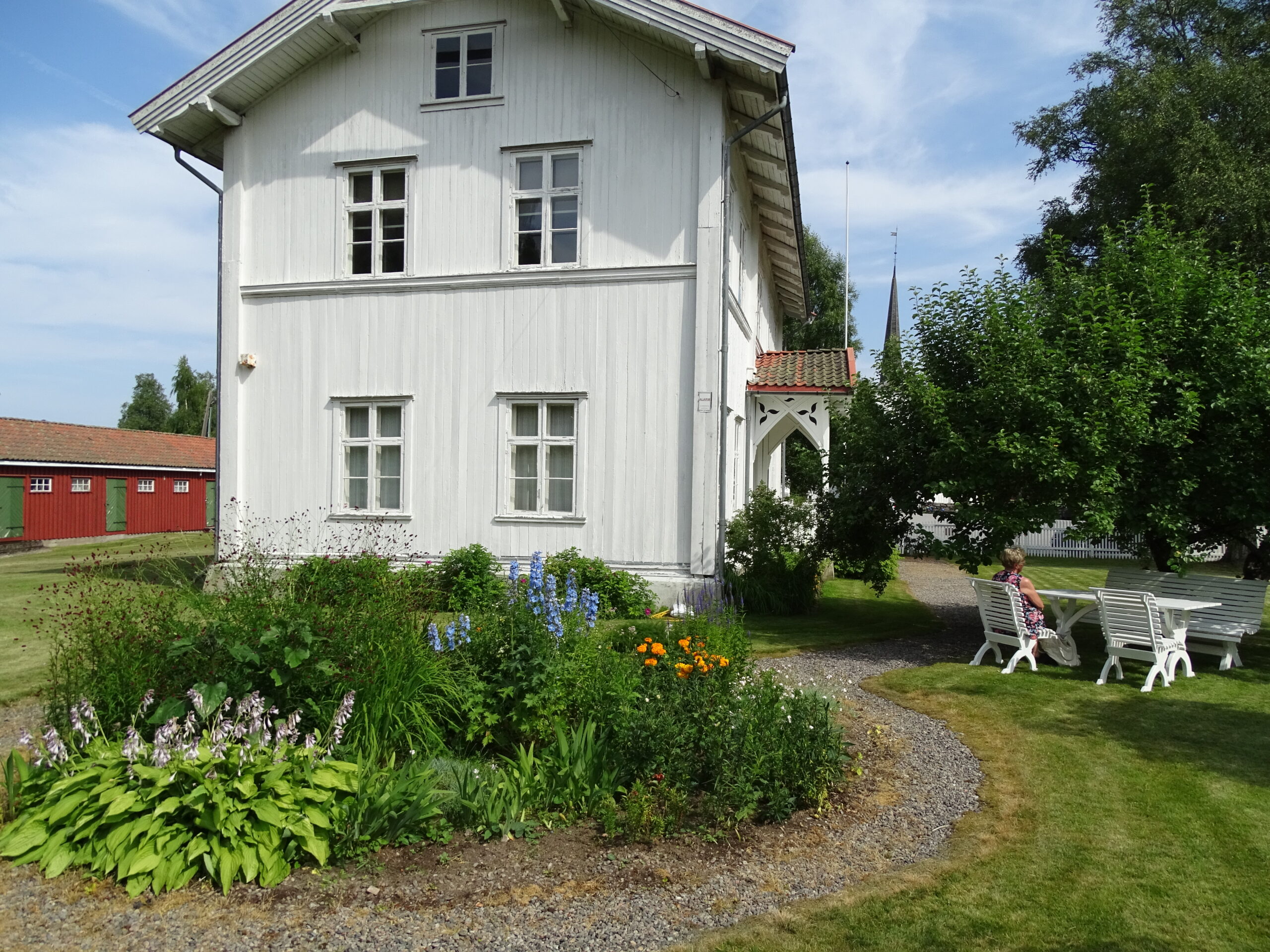 Museumsguiden nyter sola under epletreet og lar staudebedet stjele glansen utenfor skolemuseet på Matrand.