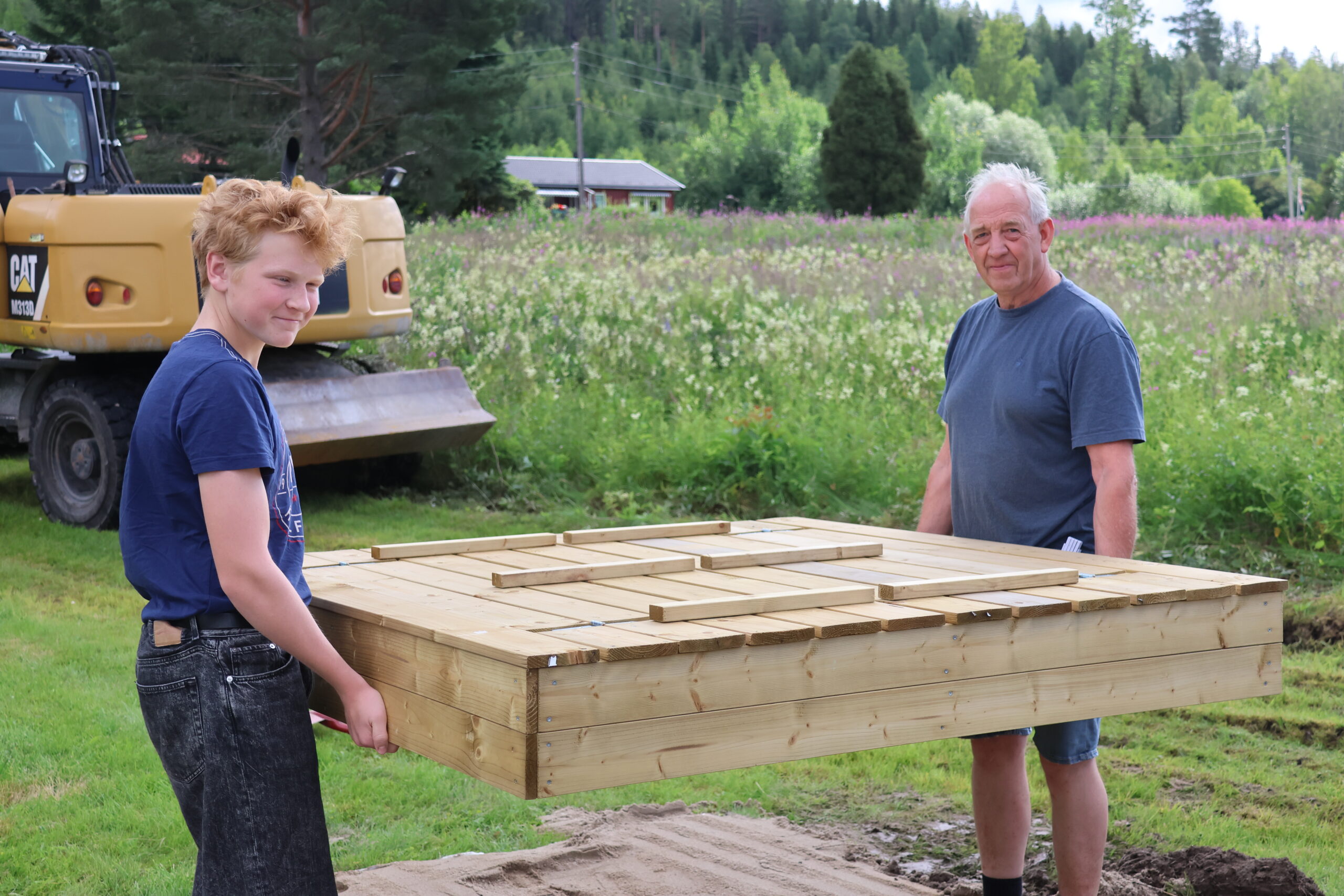 Magnus Wik Johansen (t.v) og Tormod Hansen løfter på plass den nye sandkassa.
