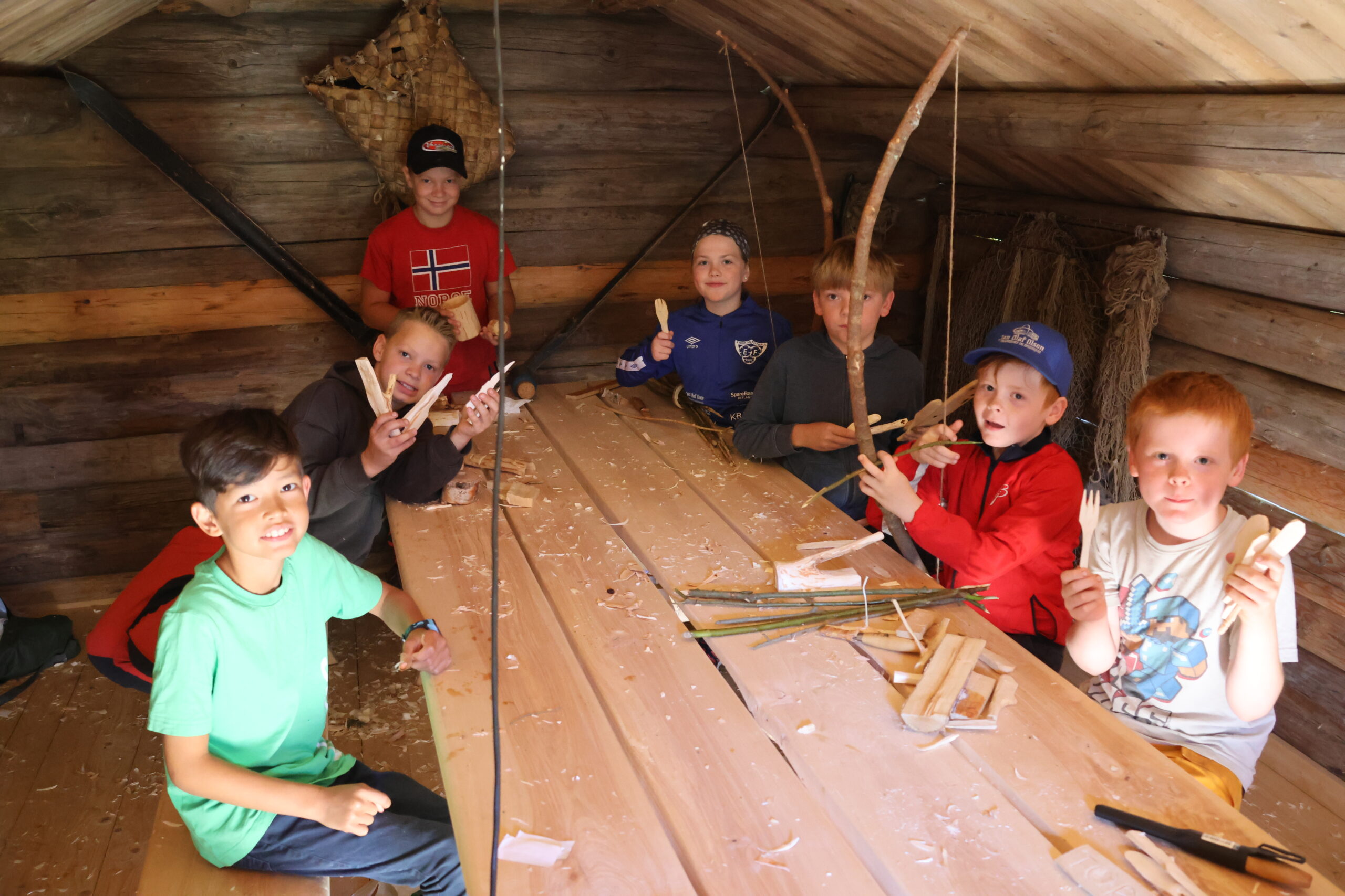 Inne i "snikkerbua" har ungene spikket både kniver,skjeer, pil og bue og andre saker. Chrstoffer Utgården ( f.v forrerst) , Martin Brøderud, Thomas, Brøderud, Eira Nordal, Øyvind Sørli, Hroar Gomsrud og Thor Kristian Gomsrud har lært mye i løpet av uka.