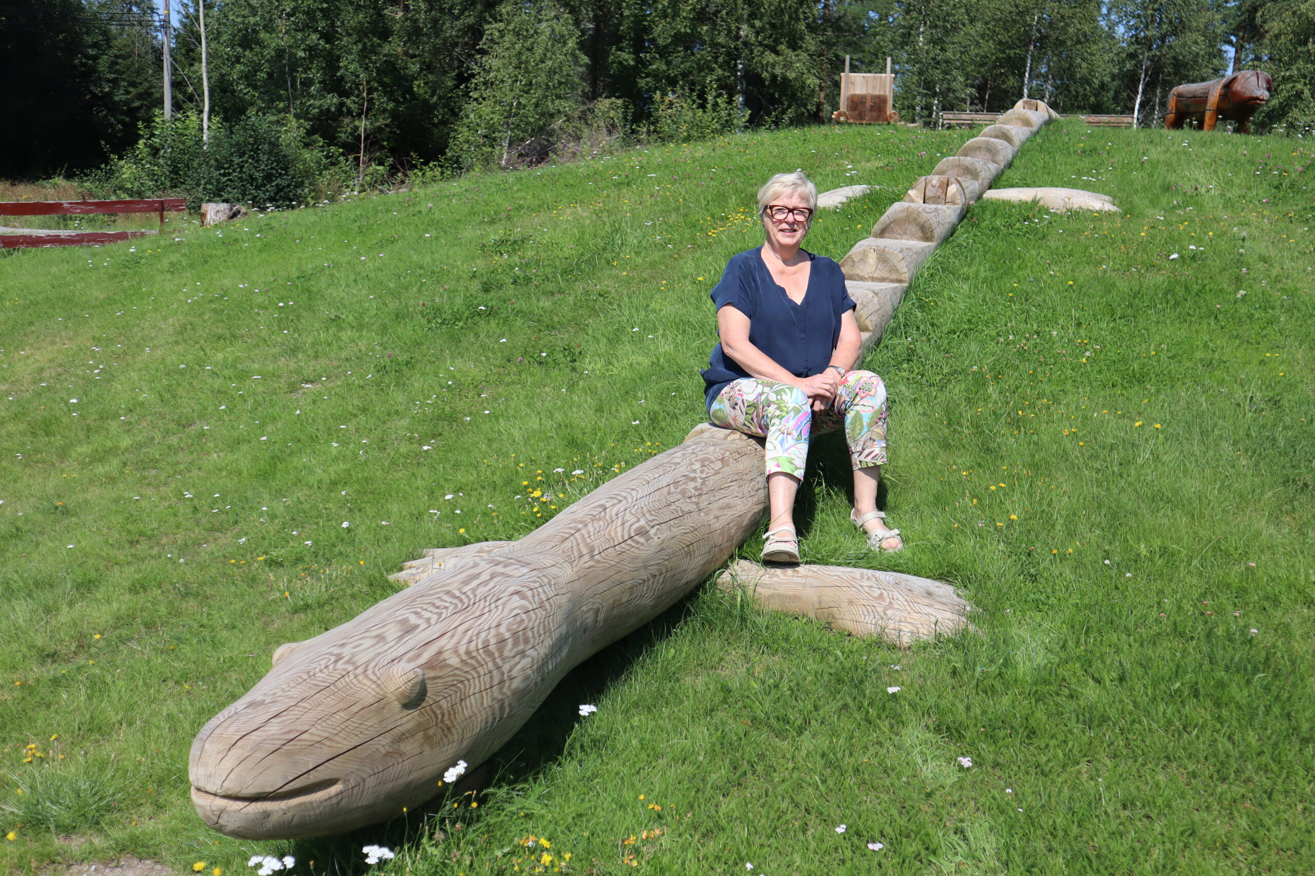 Ved Bøndenes hus på Skotterud har bygdekvinnelaget i samarbeid med Tor Nilsson, installert vakre tømmer figurer på tomta. Her sitter hun på den store firfisla.