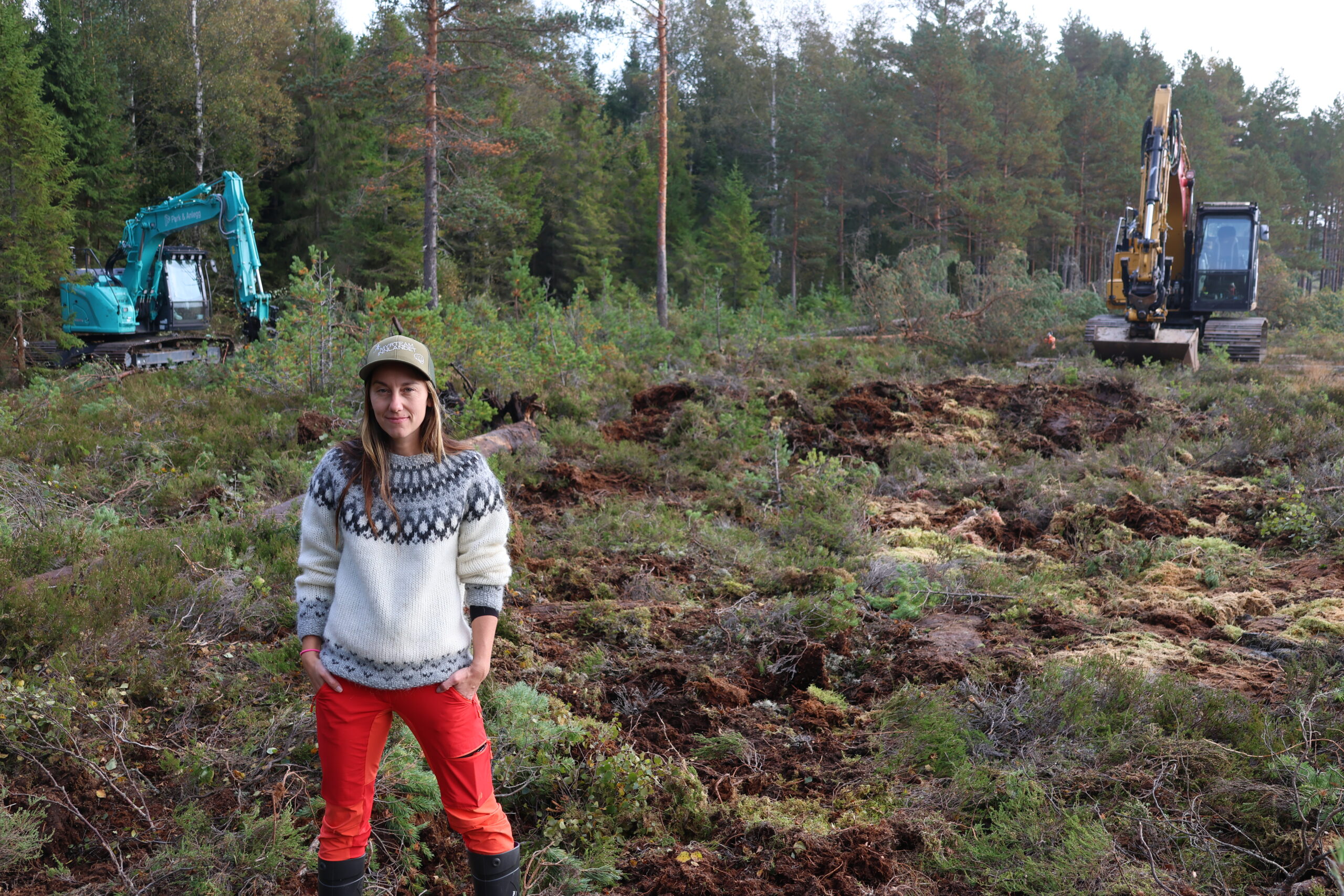 To gravemaskiner utfører det tunge arbeidet med å tette de grøftene som en gang ble gravt ut i et forsøk på å gi mer areal til å plante skog. Suzanne Wien fra Statsforvalteren sier man kan forvente å se endringer i økologien i løpet av noen år. Men at vannet vil være tilbake i myra nesten umiddelbart. Mellom henne og den gule gravemaskinen i bakgrunnen kan man se en av de nye demningsvollene som bygges for å holde på vannet.