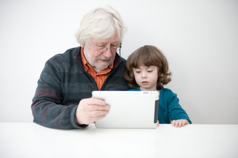 En bestefar viser barnebarnet sitt noe på en ipad.